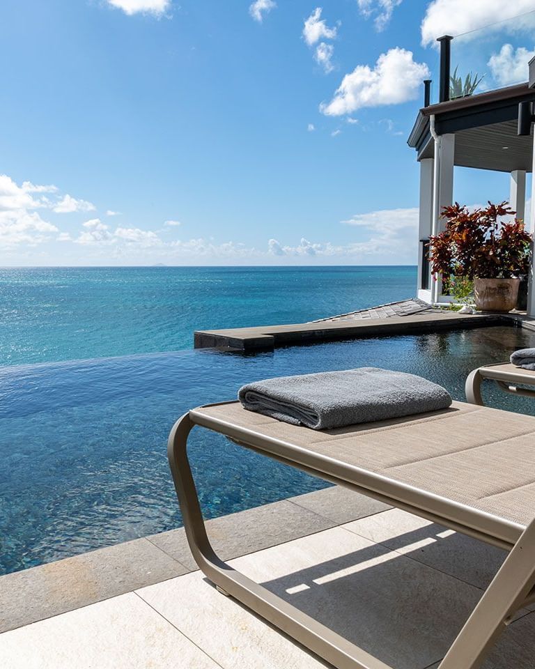 Stylish loungers on a private balcony overlooking a vast turquoise sea under a clear sky.