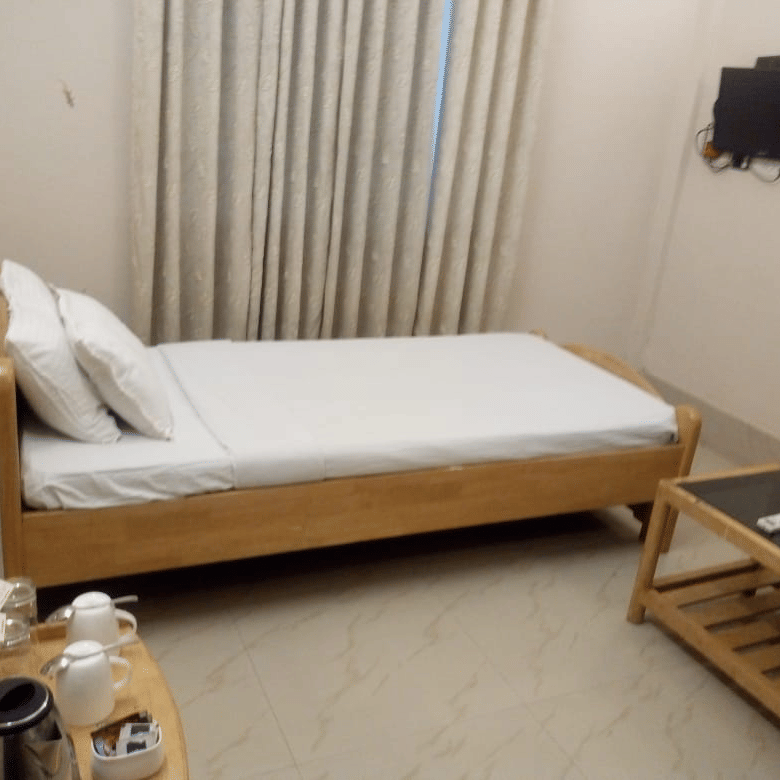 A room at Lake Side Resort Neermahal, featuring a single bed, bedspreads, a pillow, and a table.