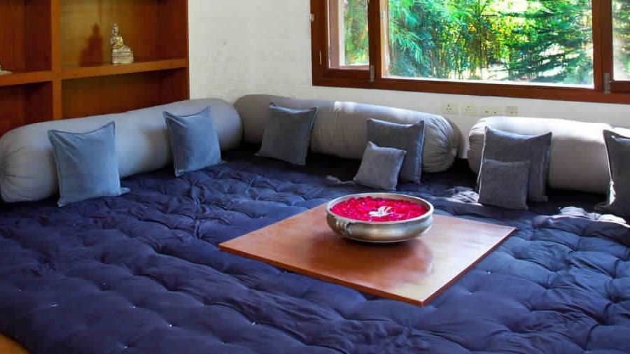 A room with a dark blue quilted floor cushion, gray cushions, and a wooden table - Shreyas Retreat