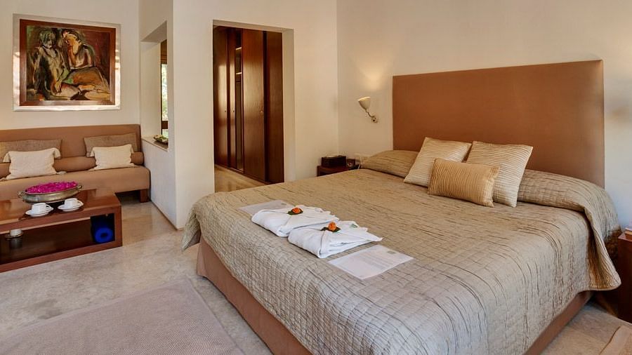 A wide angle image of a bedroom featuring a king size bed and a seating area with a cosy sofa - Shreyas Retreat
