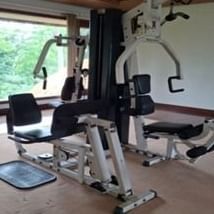 An empty home gym with a multi-station exercise machine and a large window overlooking trees