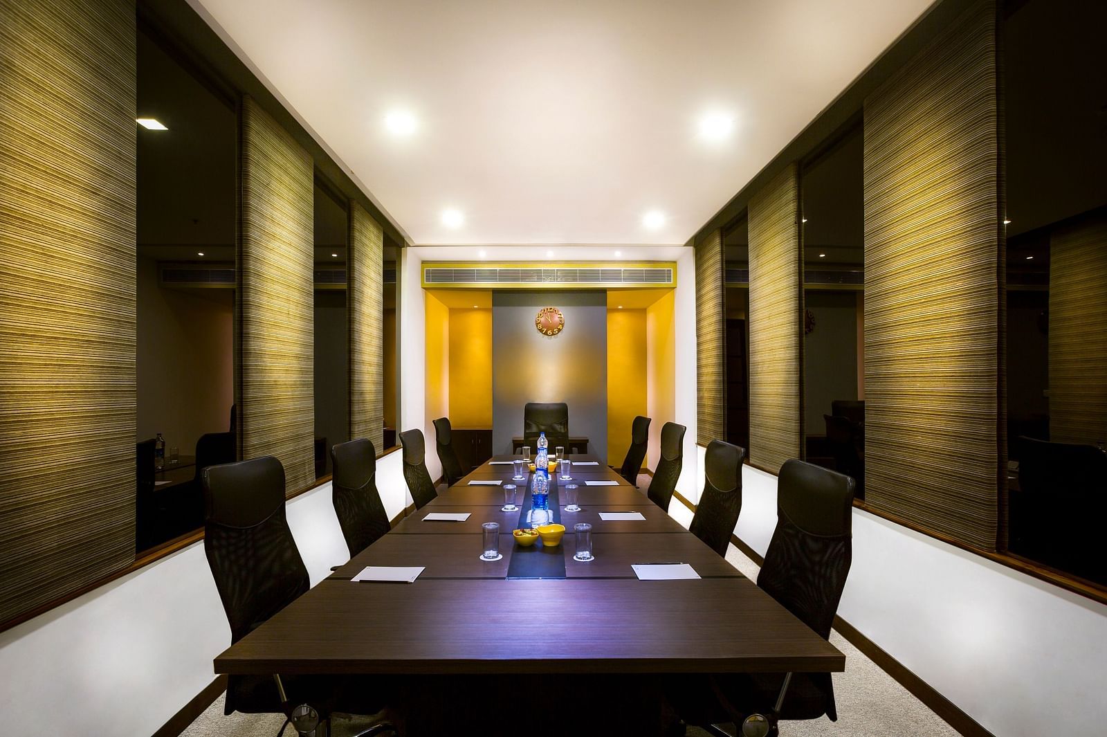 Modern meeting room with a long, rectangular table surrounded by black leather chairs. The room has neutral walls and ample lighting.