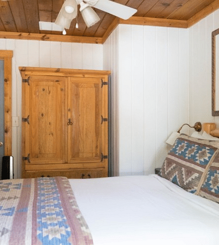 Overview of a Room at Shaver Lake Village Hotel with a wooden armoire, patterned pillows on a bed, a bear silhouette artwork, and a grey door.