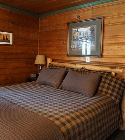 a Bedroom at Shaver Lake Village Hotel with a wooden bed frame, plaid bedding, wood paneled walls, and framed artwork.