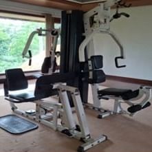 An empty home gym with a multi-station exercise machine and a large window overlooking trees