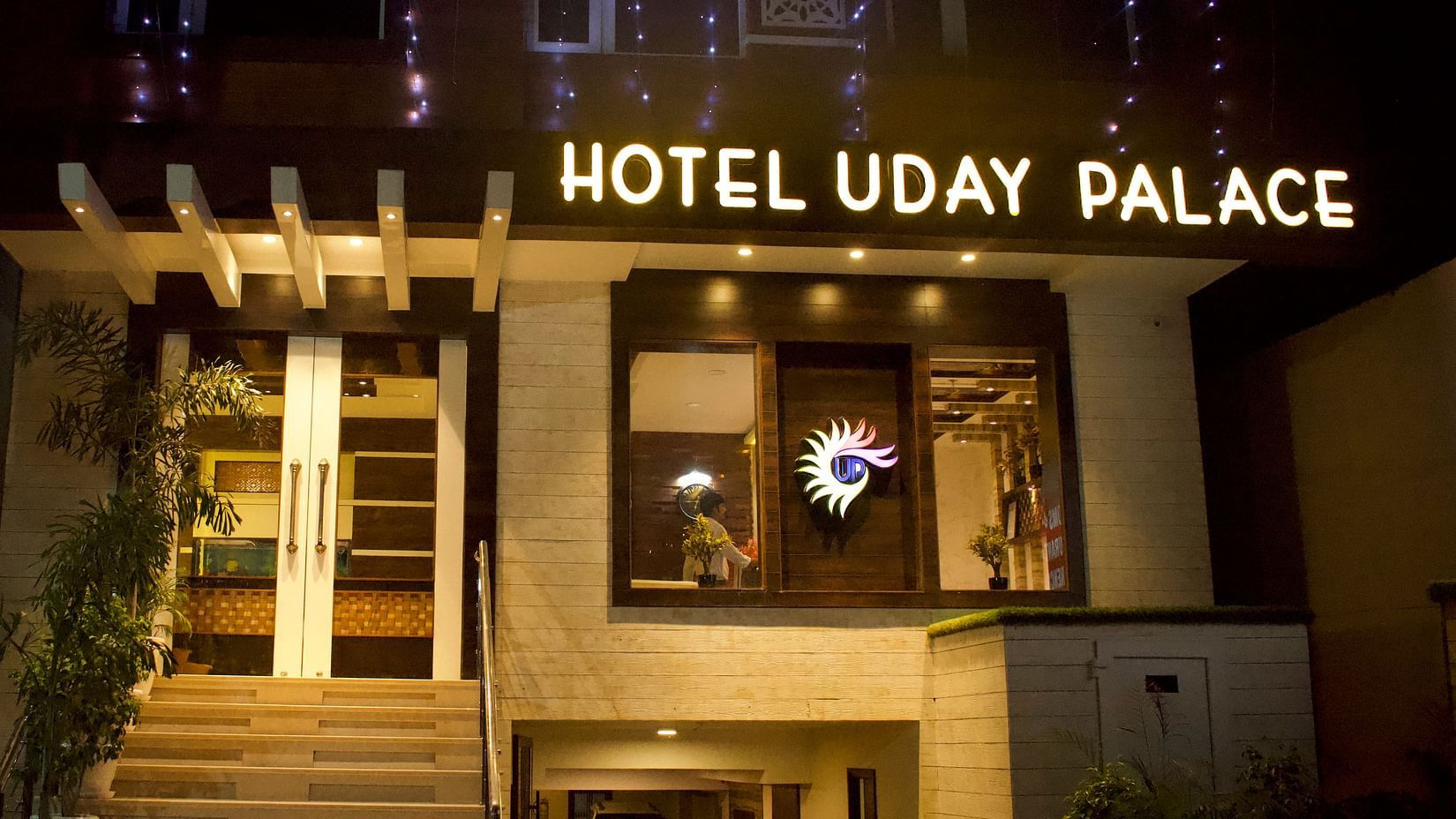 The entrance of Hotel Uday Palace with a signboard displaying the hotel’s name, illuminated by warm and welcoming lighting.