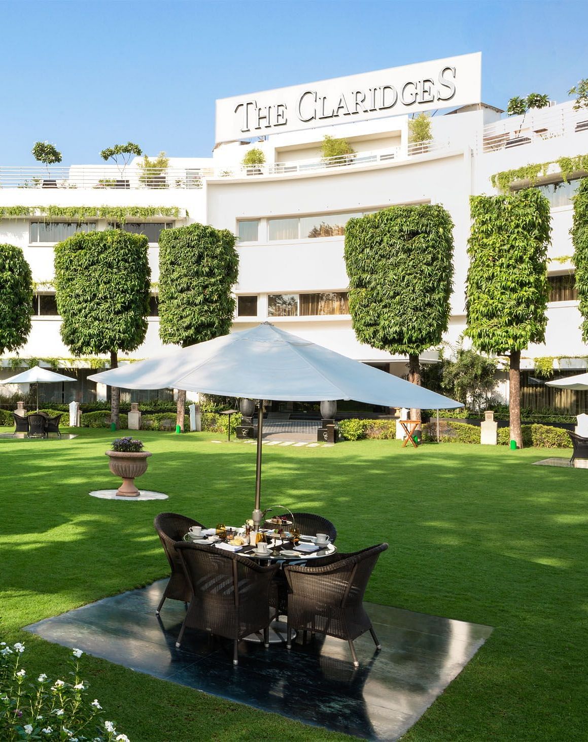 Facade of The Claridges New Delhi, featuring a green garden in the front and surrounded by towering trees, offering a serene and elegant ambience