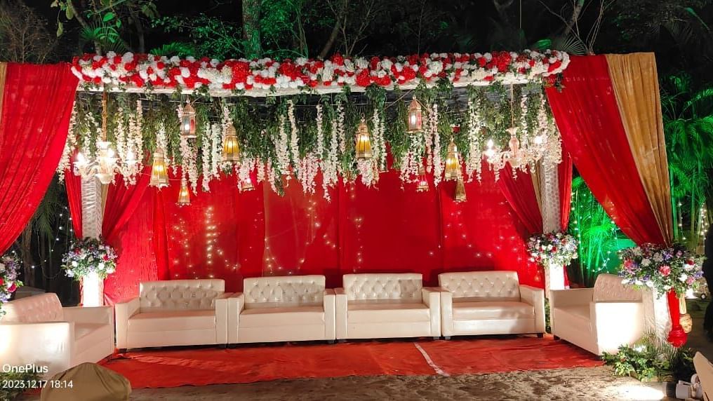 A red and white wedding stage with a comfortable seating arrangement is decorated with hanging floral garlands and drapes