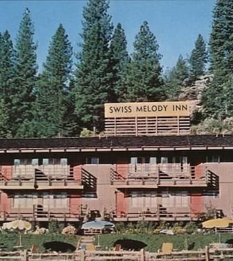 A view of the facade of Narrow Gauge Inn with a backdrop of the forest against blue skies.