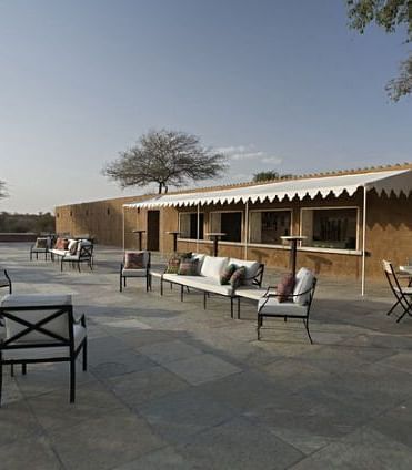 A facade image of the outdoor seating area with chairs and the resort in the background - MANVAR Resort & Desert Camp