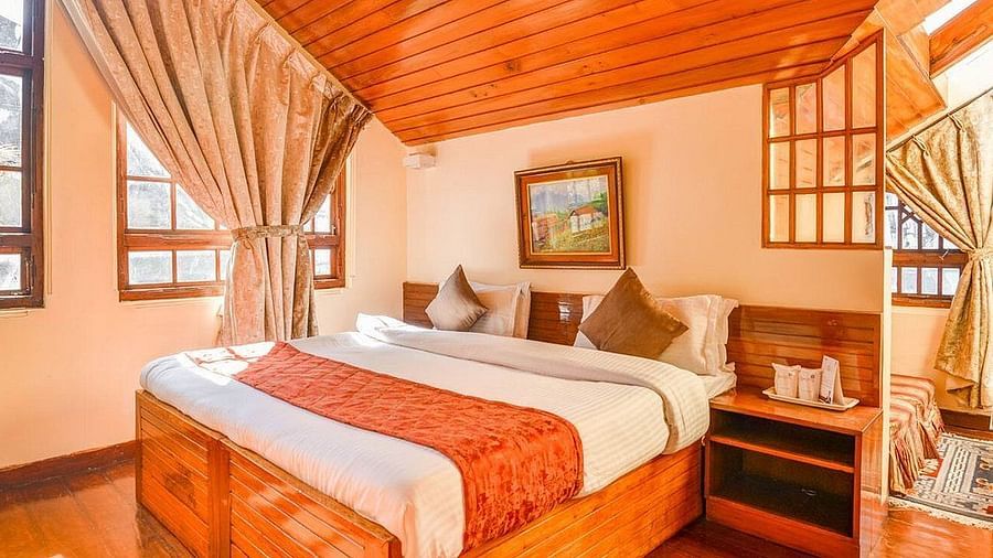 A suite room, featuring a spacious bed positioned adjacent to expansive windows adorned with curtains, while mirrors adorn another side at Sumitel Oriental, Gangtok.