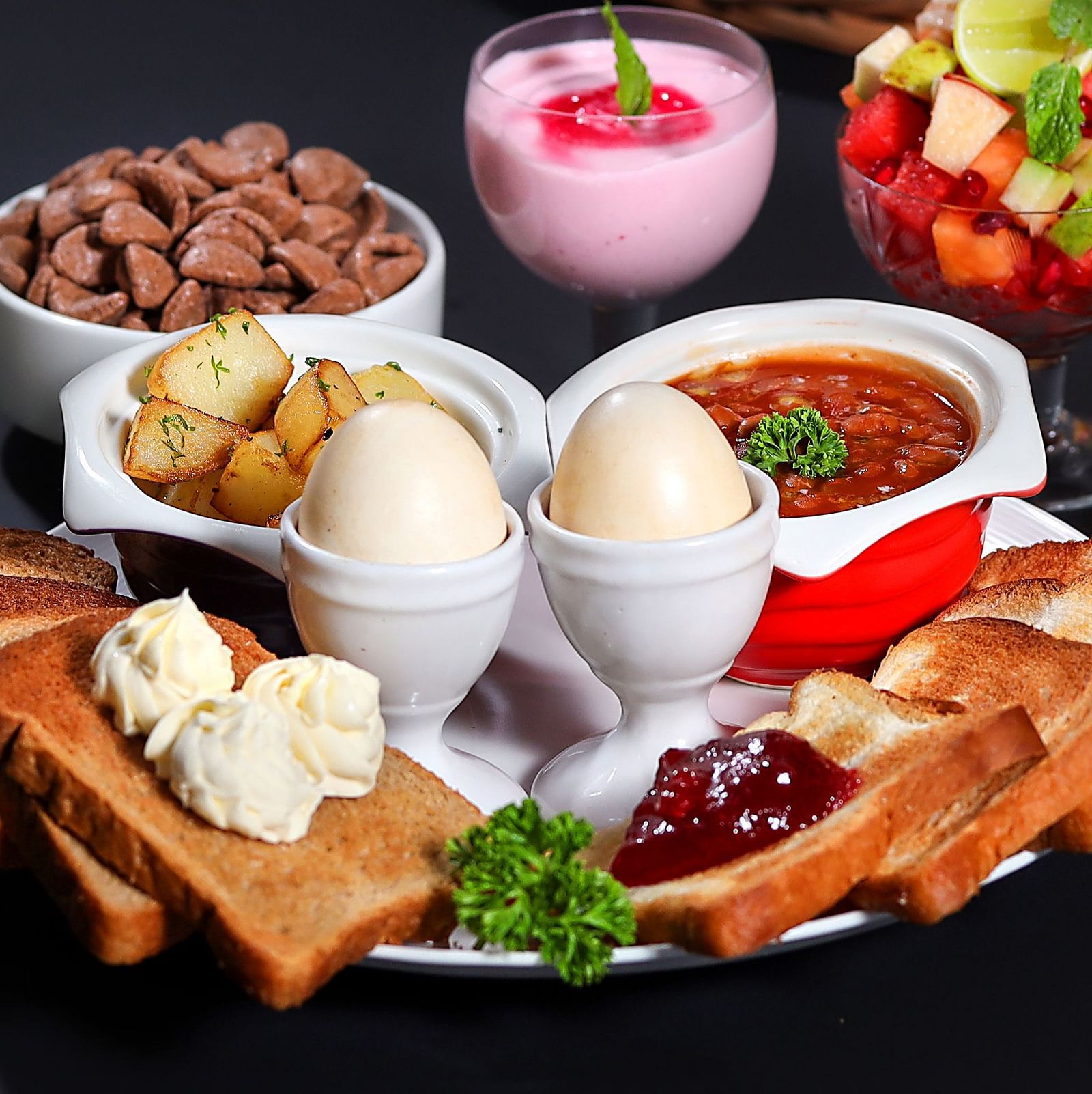 image of a vast platter of breakfast items well kept on a plate featuring 2 eggs in egg stand along with toasts and various other things