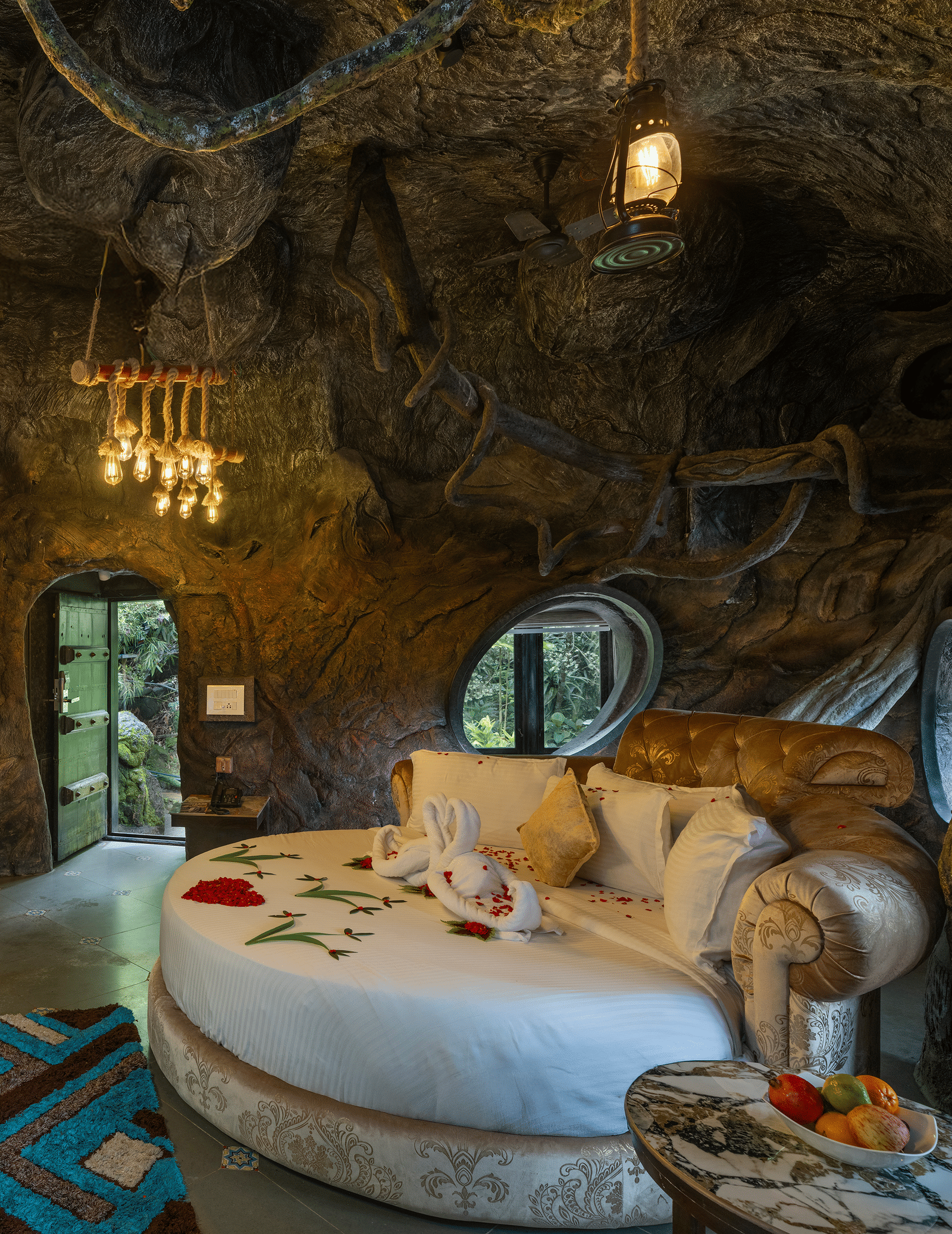 The bedroom of the Cave Room at Parakkat Nature Hotel and Resorts, Munnar, featuring a large circular bed, decorative light fixtures, and walls designed to resemble natural rock formations.