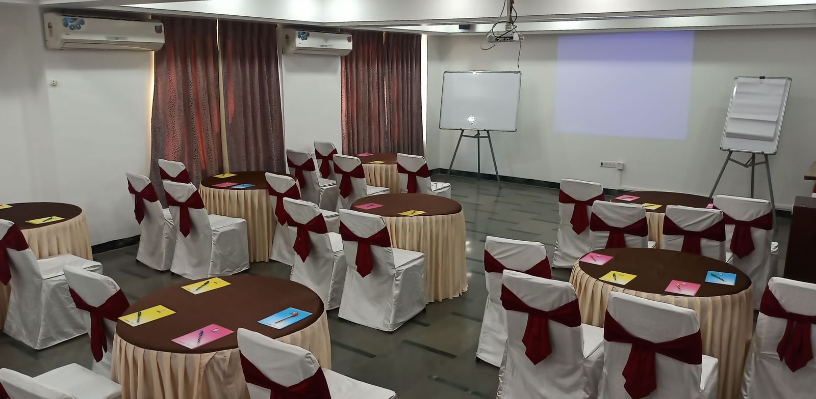 Training room setup with cluster seating arrangement, notepads, and a projection screen at Mayur Retreat.