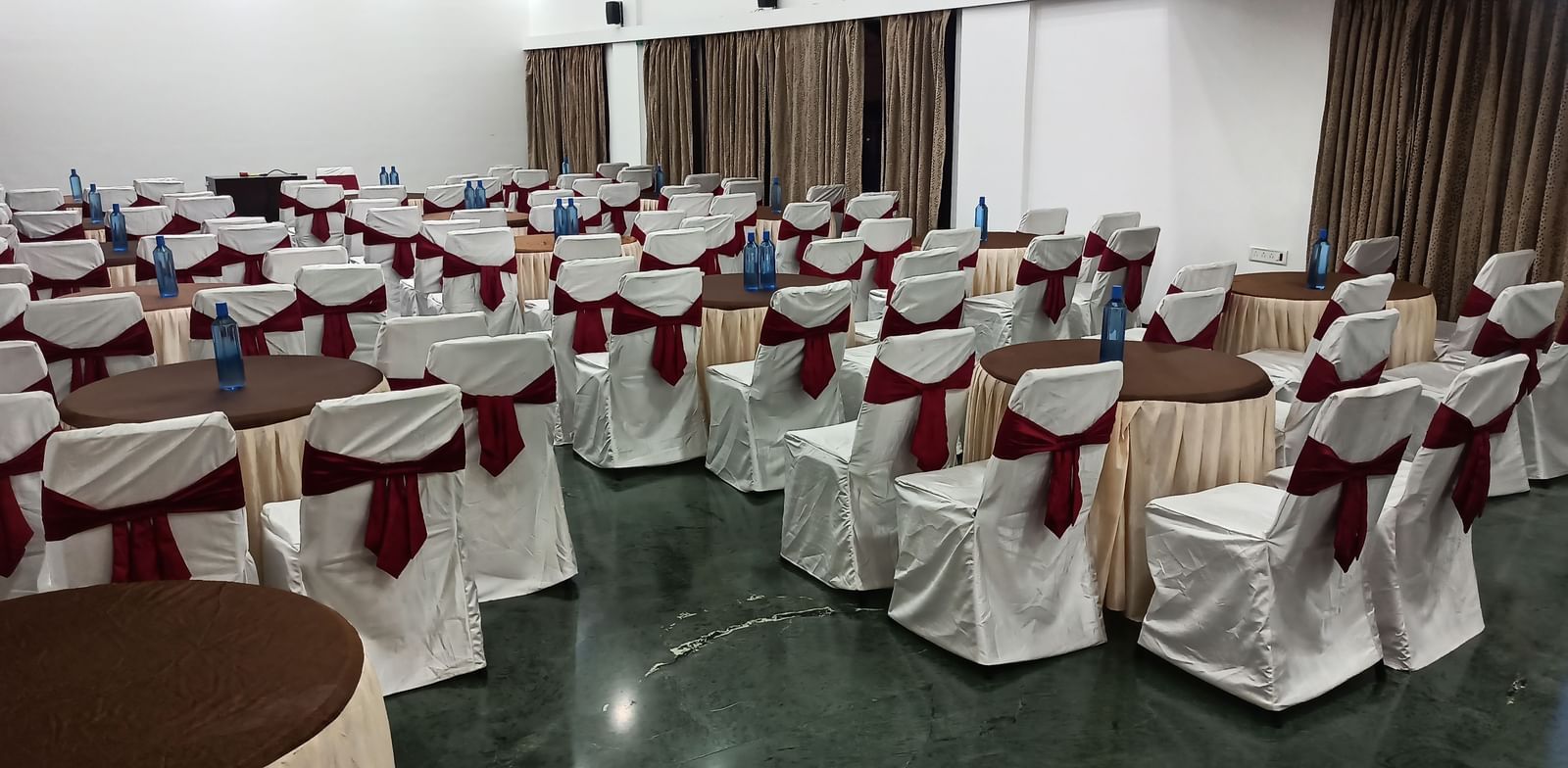 Cluster seating arrangement with white covers and maroon chair sashes, suitable for formal dining or events at Mayur Retreat.