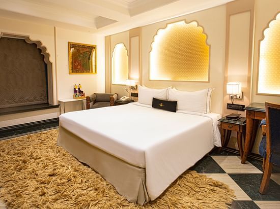 A side angle view of a Rajasthani-themed bedroom featuring a plush bed and beautiful decor, highlighting the rich colors and intricate details.