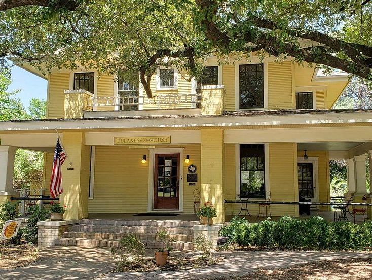 A beautiful house with a front porch, surrounded by trees, and an inviting entrance.- The Grand Hotel & Ballroom, McKinney