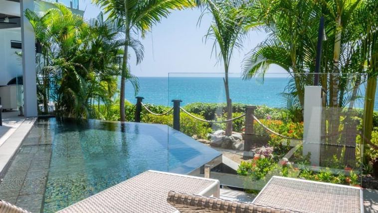 A luxurious infinity pool with lounge chairs, surrounded by lush tropical plants, with a clear view of the ocean.