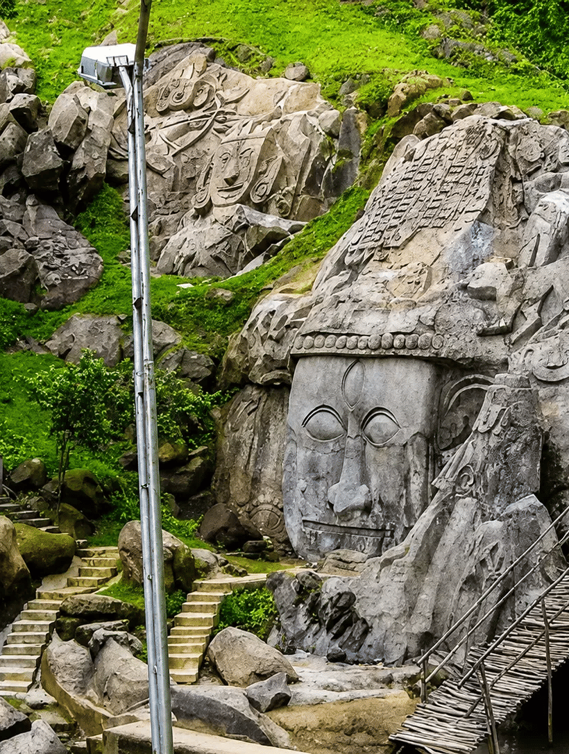 Old rocks with faces of the god carved and a tall pole infront of it.