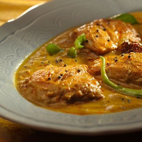 Creamy fish curry with spices and chili garnish.