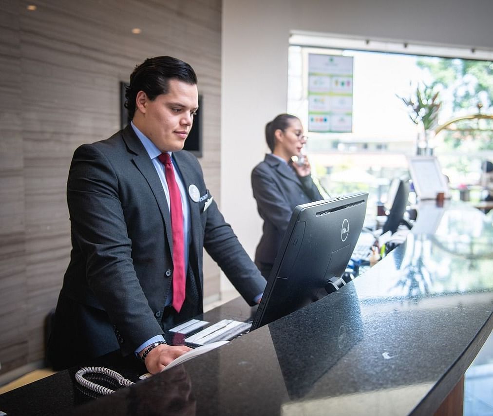 Two staff members standing behind the reception desk dressed in business formals.