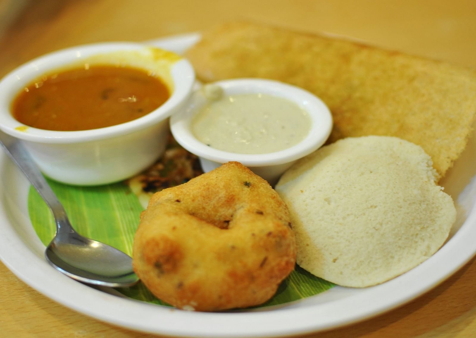 A close up shot of a plate consisting of South Indian breakfast items including idli, vada and dosa.