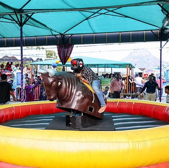 A kid rides a mechanical bull at Ramoji Film City with onlookers nearby.