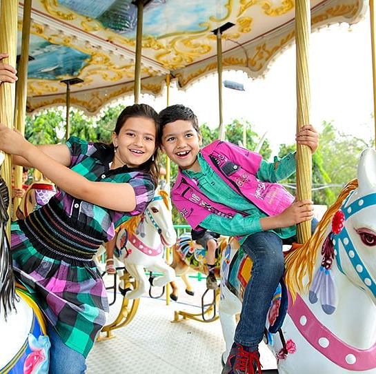 Two smiling children enjoy riding a carousel at Ramoji Film City.