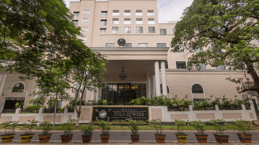 Polo Hotel, Agartala exterior with cream multi-storey facade, central porte-cochere, white boundary wall with hotel name signage and potted plants.