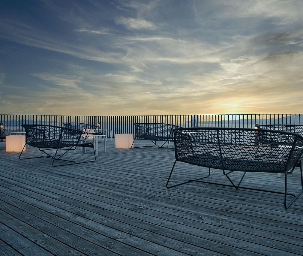 A terrace featuring a wooden deck with a few benches facing towards the beautiful sunset.