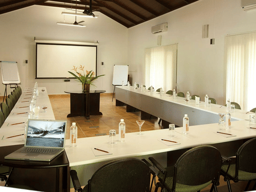 Conference Hall in Bandipur at The serai Bandipur with a U-shaped table and a projector screen under warm lighting