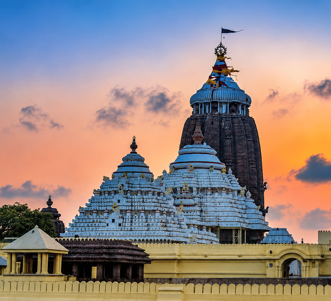 Jagannath Temple in Puri with tiered white and brown spires, a crowning flag and boundary wall at sunset, near MAYFAIR Palm Beach Resort, Gopalpur-on-Sea.