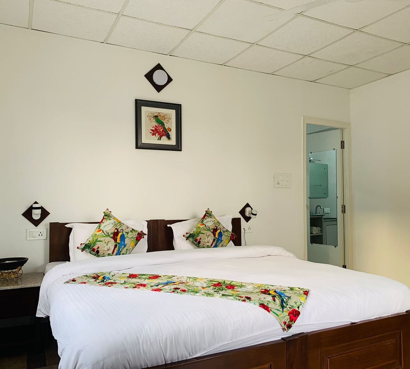 a double bed with pillows, side tables and a bed runner on it inside one of the rooms - Neer Ganga Resorts