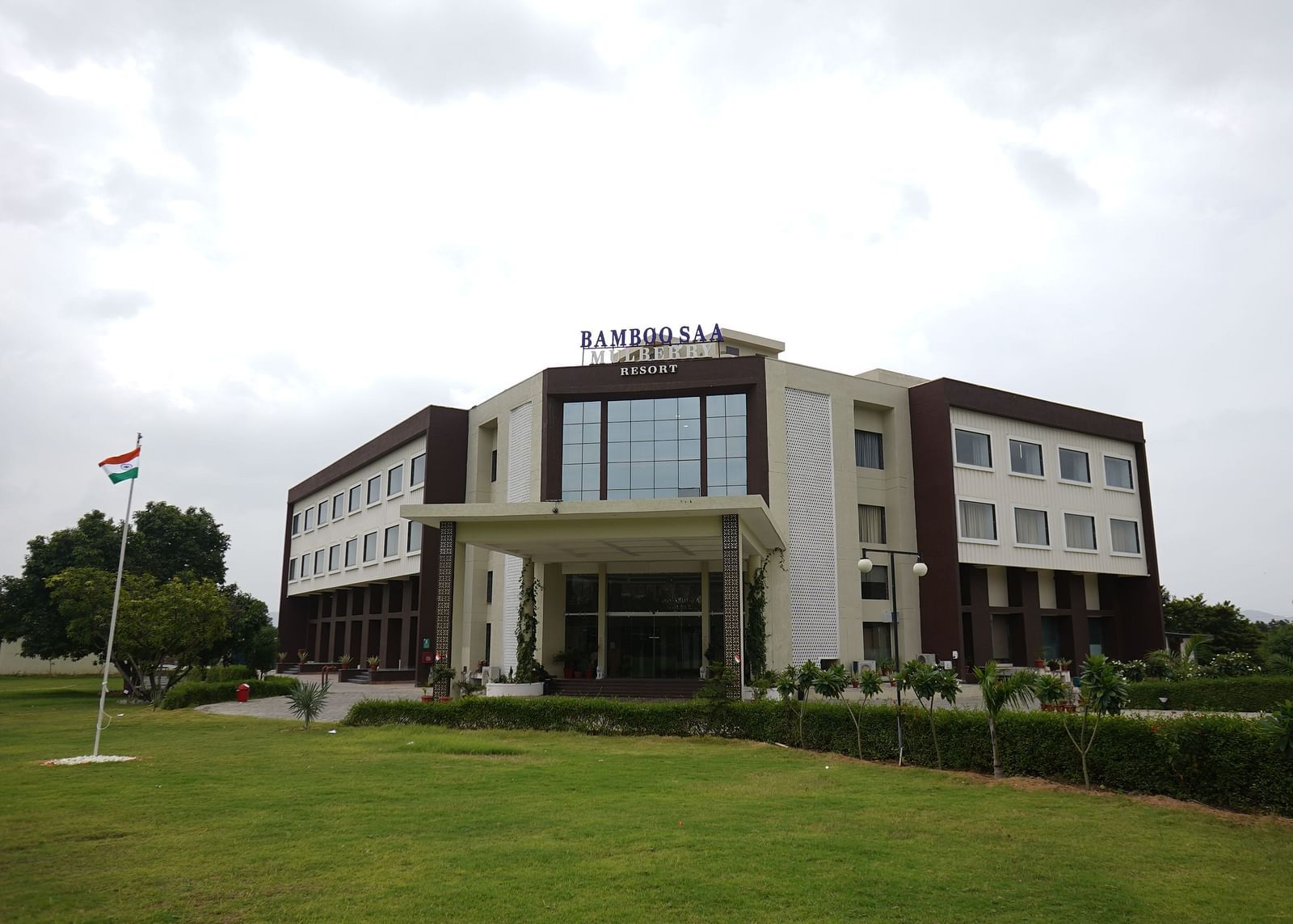 Exterior view of Bamboo Saa Mulberry Resort, Pushkar, Rajasthan featuring a modern building with a light-coloured facade with a lawn in the foreground