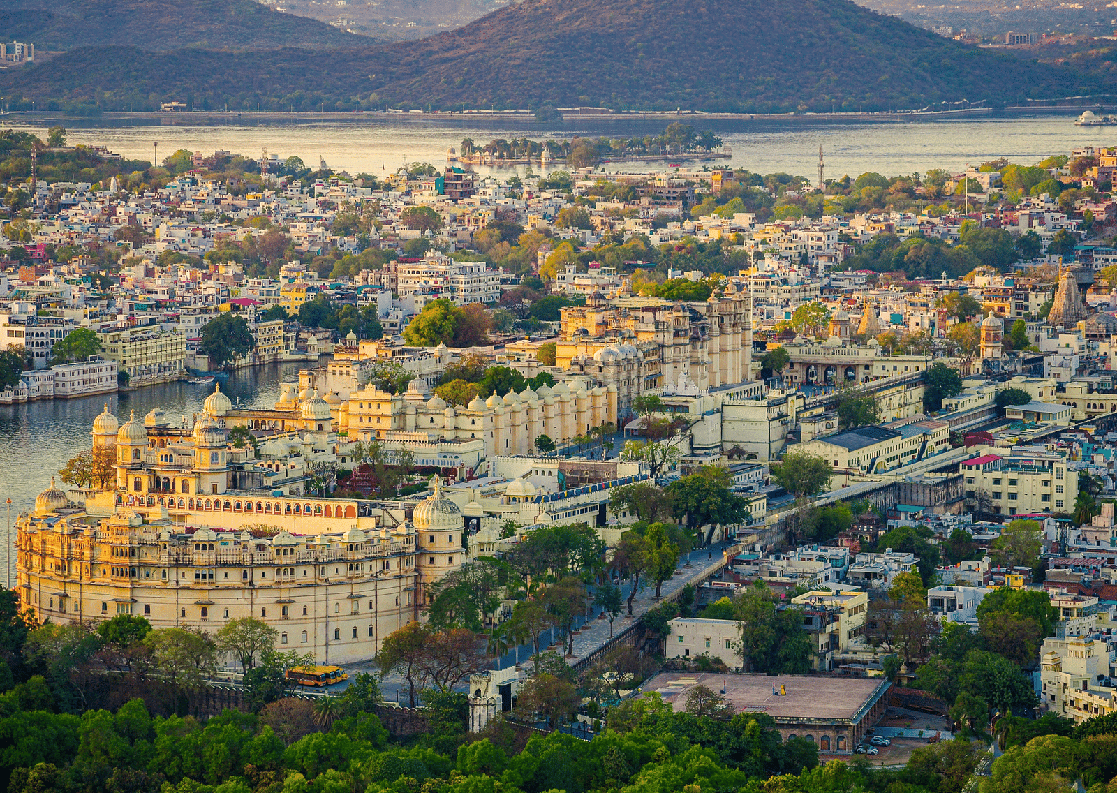 An aerial view of a sprawling city nestled along a lake, with mountains in the background.