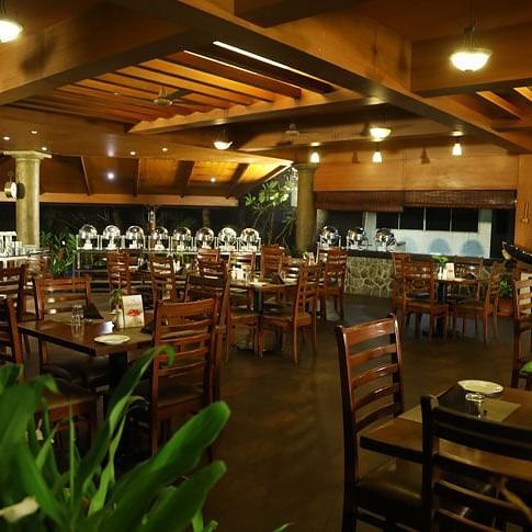 spacious and warmly lit Southern Express at Uday Suites features numerous unoccupied wooden tables and chairs, with buffet stations at the back