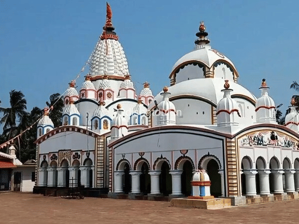 The bright white Chandaneshwar Temple featuring ornate domed towers, curved arches, and decorative colourful accents set under a clear blue sky.