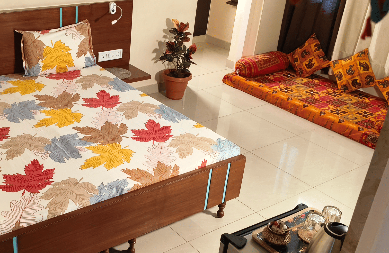 A bedroom with a double bed, floral bedsheet, side tables and a small seating area with cushions at Jaypore360 Homestay - Best Homestays in Jaipur.