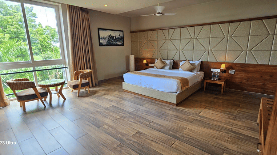 Double bed with wooden floor and seating area near windows at Cholaa Dynasty, Kumbakonam.
