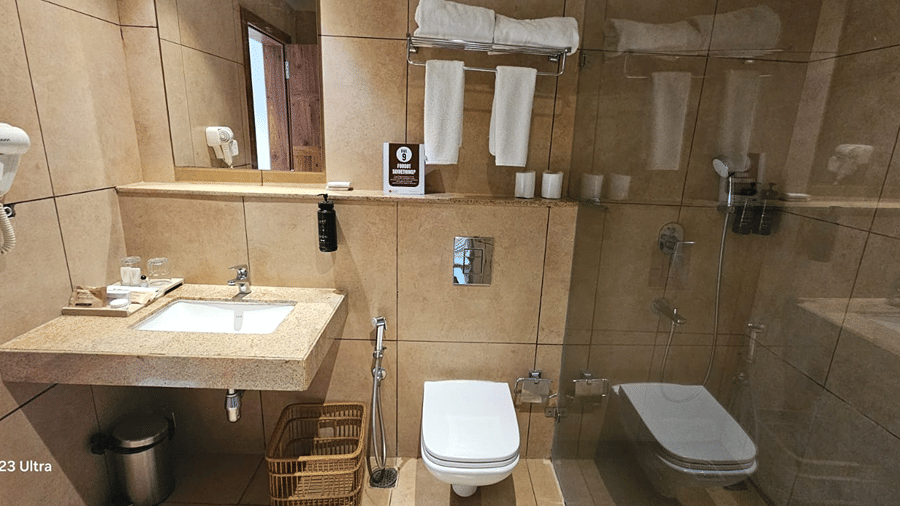 Bathroom with a washbasin, toilet, and wall hairdryer at Cholaa Dynasty, Kumbakonam.