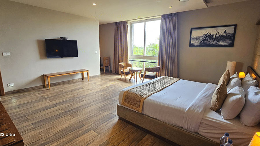 Bed with white sheets and a wall-mounted television at Cholaa Dynasty, Kumbakonam.