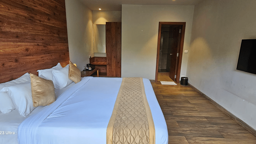 A king bed with white linen and a wooden headboard at Cholaa Dynasty, Kumbakonam.