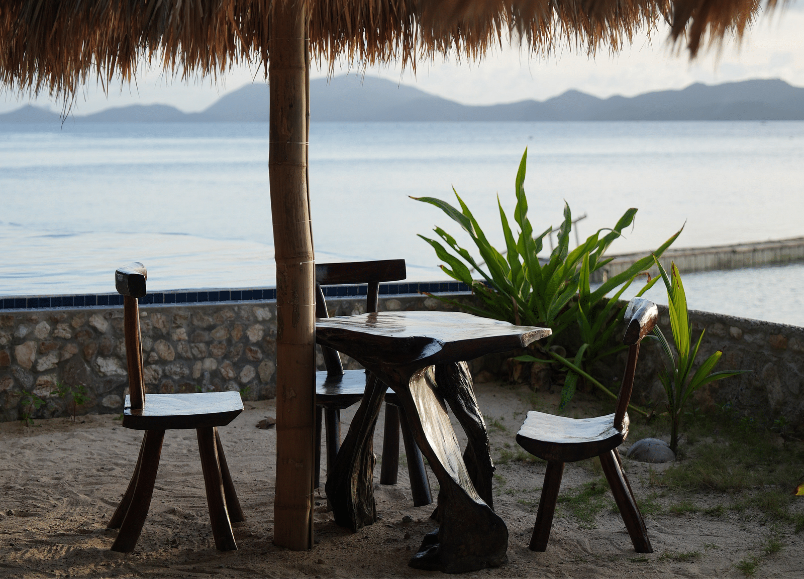 Two chairs and a table set facing the sea under a thatched umbrella at Flower Island Resort.