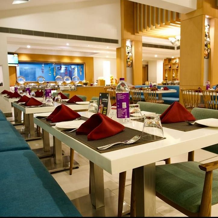 A well lit dining area of Lords Plaza Ankleshwar with buffet stations and neatly arranged tables and chairs 