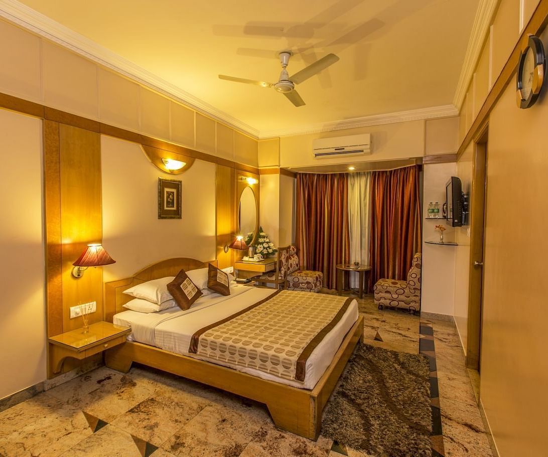 An image of a bedroom featuring a double size bed, bedside tables on either side and a seating area in one corner of the room - Hotel Pai Viceroy Jayanagar 