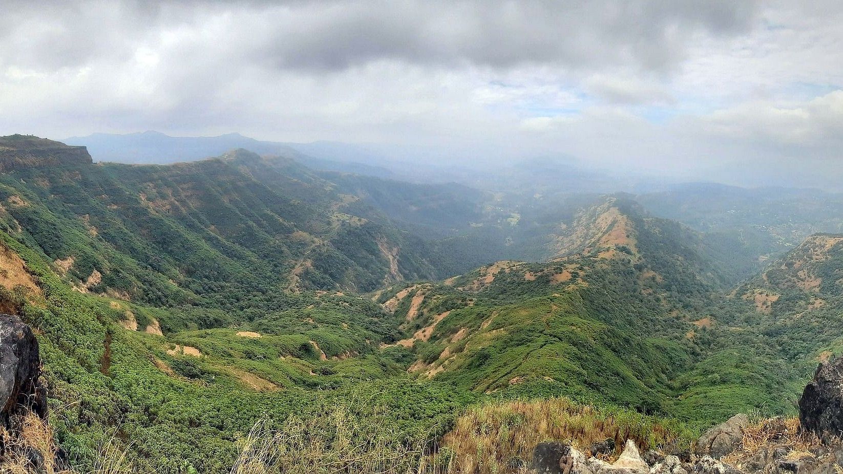 The lush landscape captured from in a birds eye view, visualised with clouds , and shot between a couple of boulders.