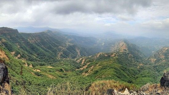 The lush landscape captured from in a birds eye view, visualised with clouds , and shot between a couple of boulders.