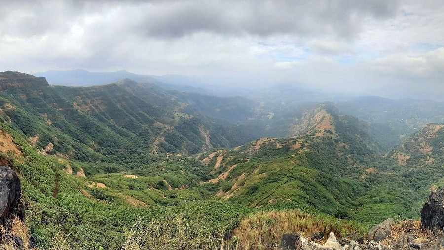The lush landscape captured from in a birds eye view, visualised with clouds , and shot between a couple of boulders.