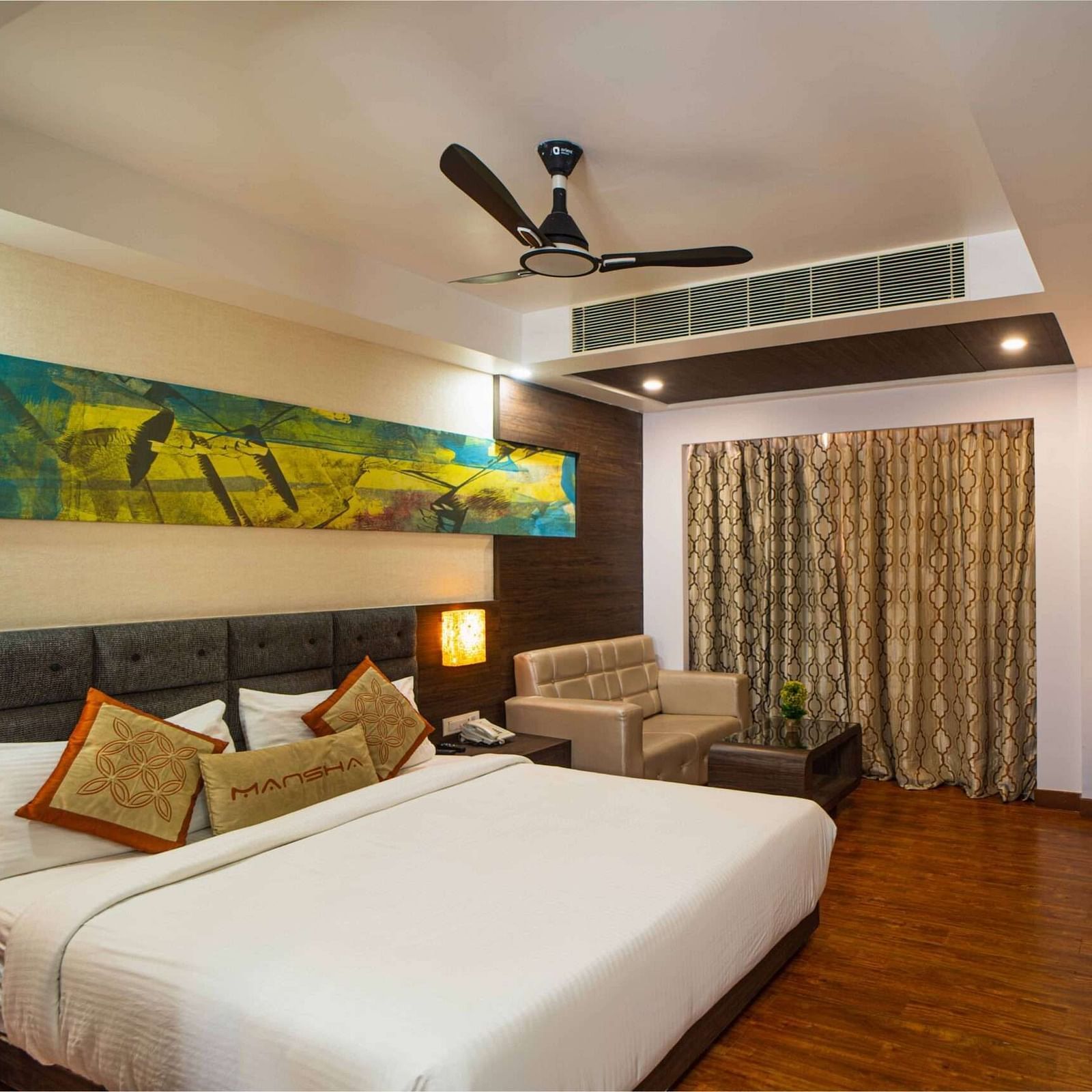 A room with a bed, a sofa, a wall-mounted television, and a ceiling fan at Mansha Hotel Regency.