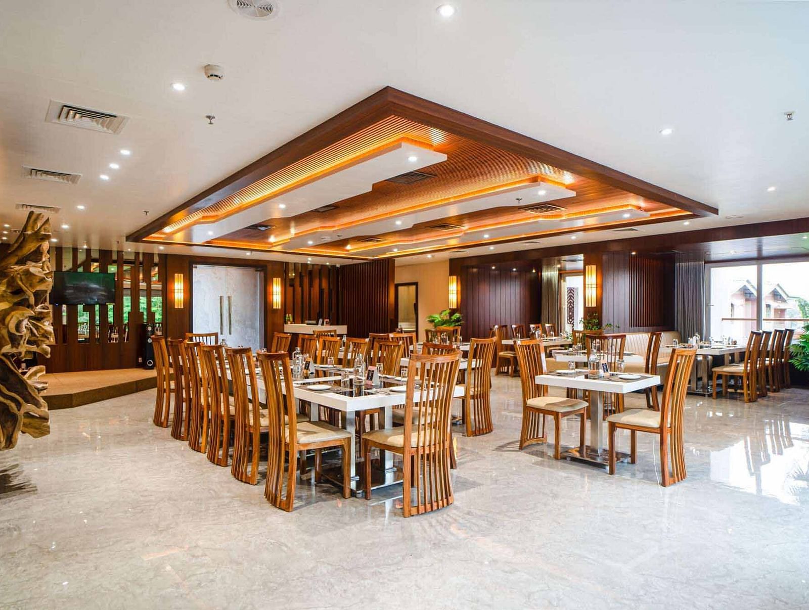 The spacious and brightly lit dining hall at Mansha Palace features numerous set tables and comfortable wooden chairs.
